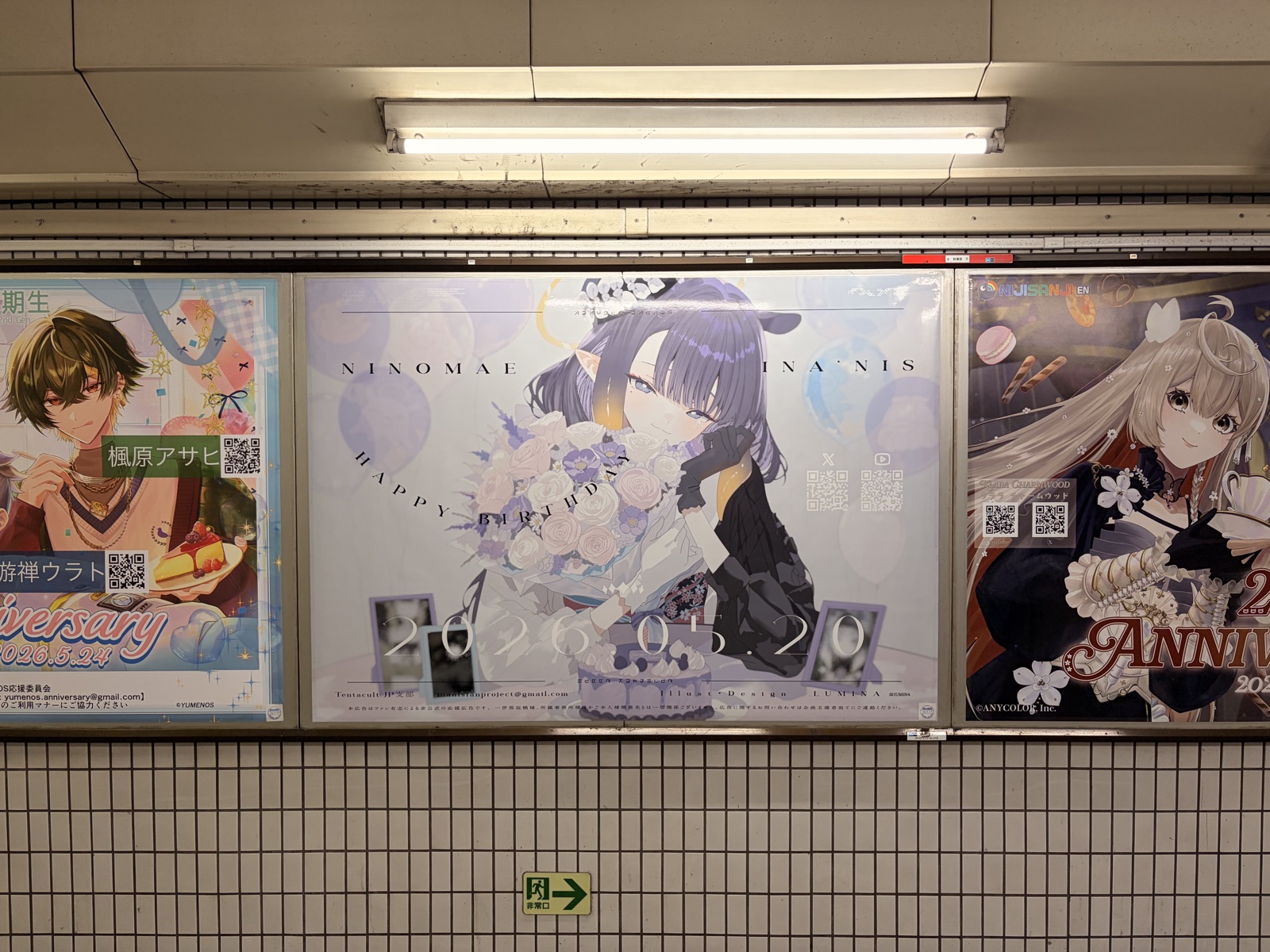 Wide view of the station wall — the Ina'nis birthday poster displayed alongside neighboring fan advertisements